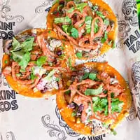 Three Talkin' Tacos with crispy onions, cilantro, and cotija cheese on branded parchment paper.