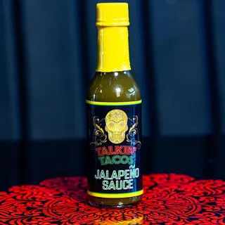 A bottle of Talkin' Tacos Jalapeño Sauce with a yellow cap and a sugar skull label.