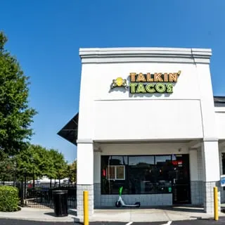 Exterior of Talkin' Tacos restaurant with outdoor seating, a scooter, and a bright blue sky.