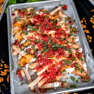 A tray of Talkin' Tacos loaded fries with cheese, red sprinkles, cilantro, and white sauce.
