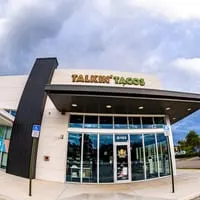 Exterior of Talkin' Tacos restaurant with its sign, large windows, and a dark, cloudy sky.
