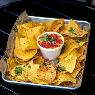 A tray of Talkin' Tacos tortilla chips with a cup of cheese dip, cilantro, and red sprinkles.