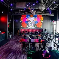 The interior of Talkin' Tacos restaurant with a large colorful sugar skull mural and empty tables.